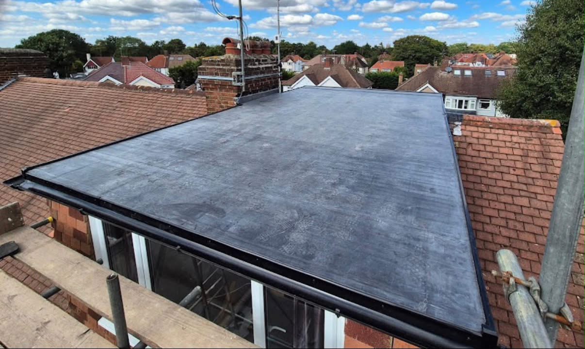New flat roof with clay tiles and a brick chimney beyond