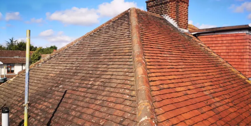 Weathered clay-tiled hip roof beside a brick chimney before replacement