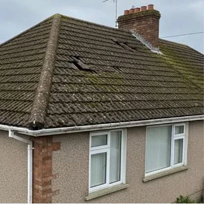 Moss-covered roof with damaged tiles beside a chimney before work
