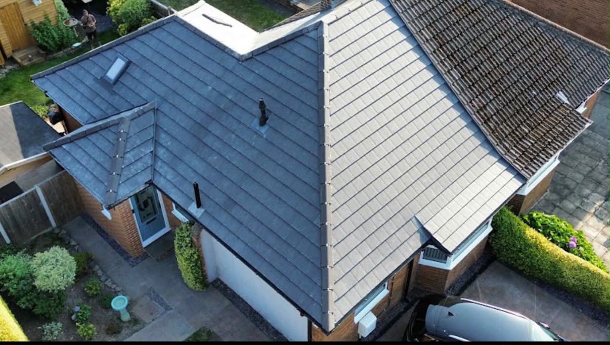 Drone view of a completed dark tile re-roof beside the original weathered roof